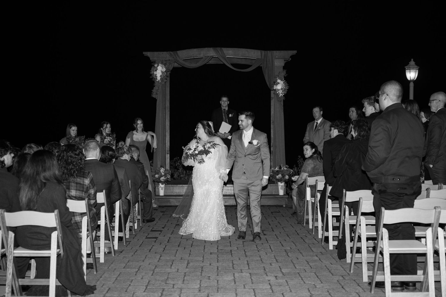 A black and white photo of a wedding ceremony processional on a brick pathway.