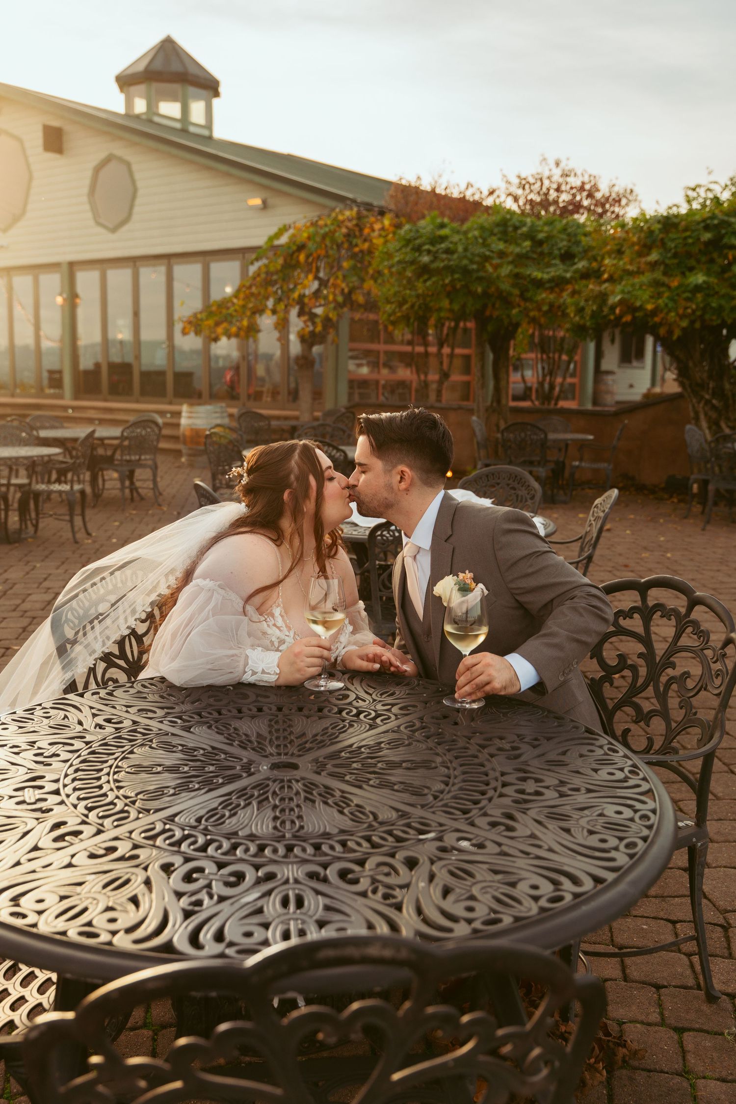 Couple leans across decorative metal patio table during golden hour at vineyard reception.