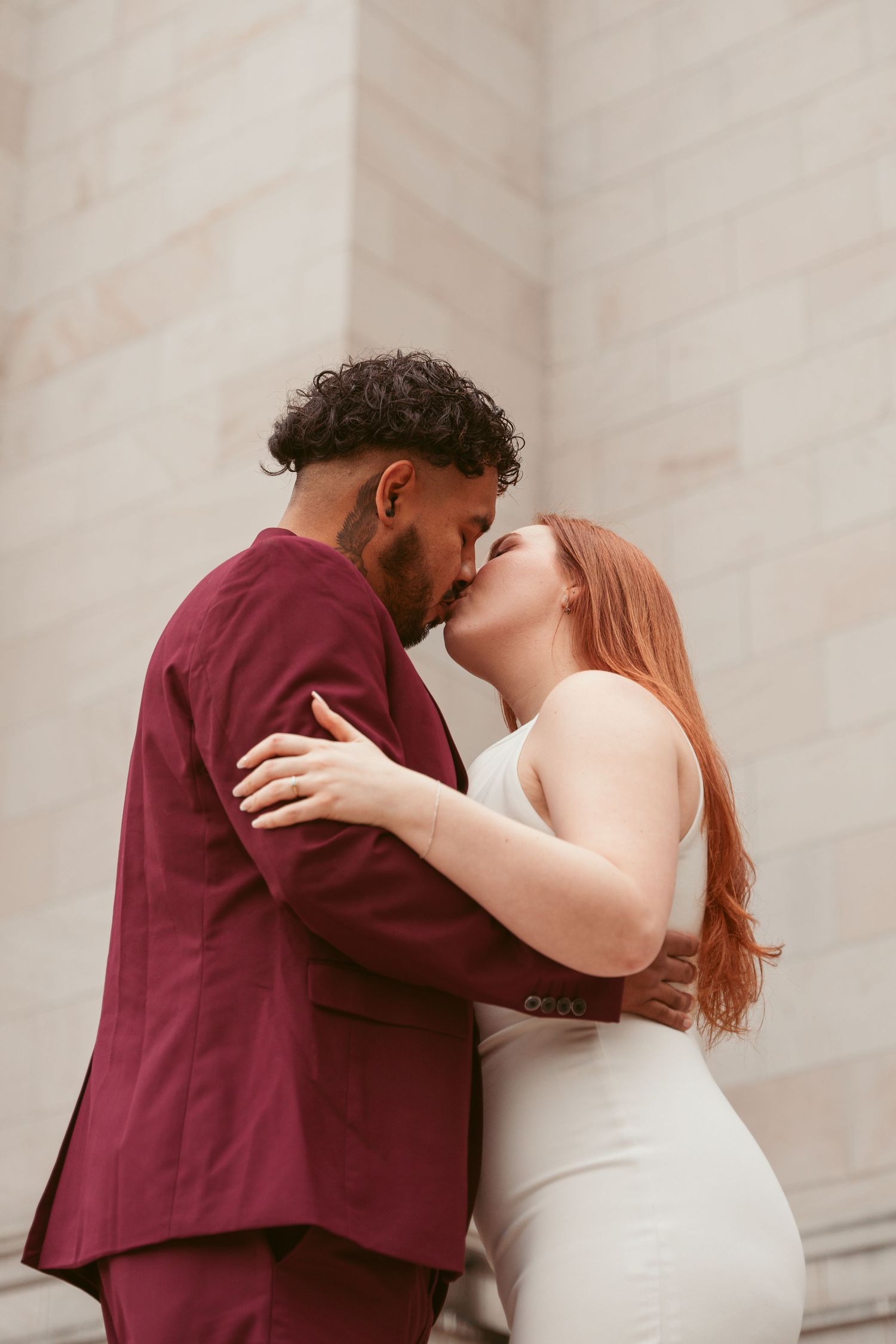 Couple embracing and kissing against a light colored wall background.