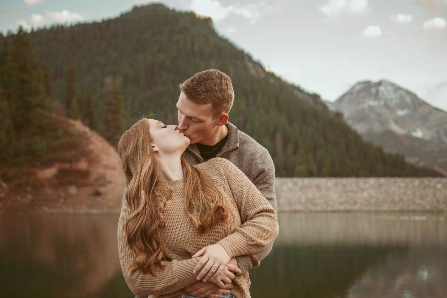 A couple shares intimate moments against a scenic mountain lake backdrop.
