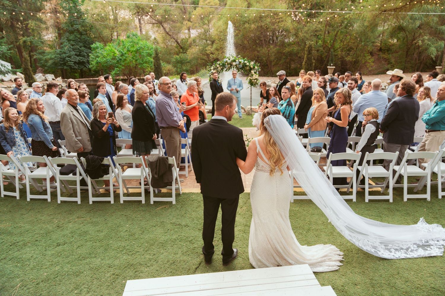 Outdoor wedding ceremony with large crowd of guests and flowing white veil.