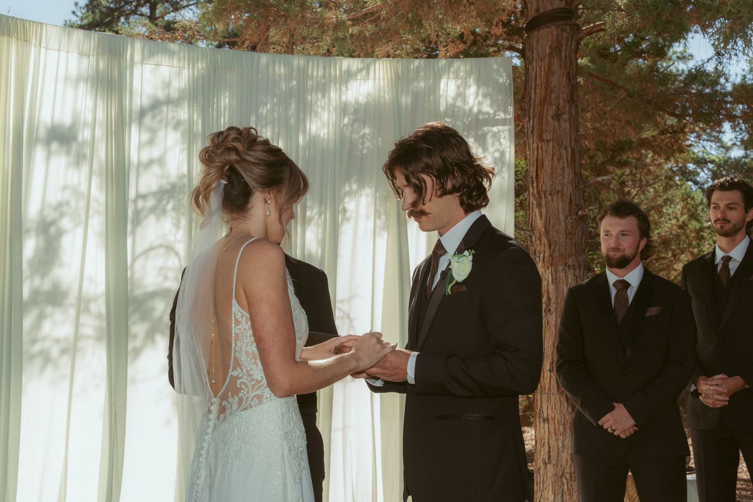 A wedding ceremony takes place in a forest setting with white curtains and natural decor.