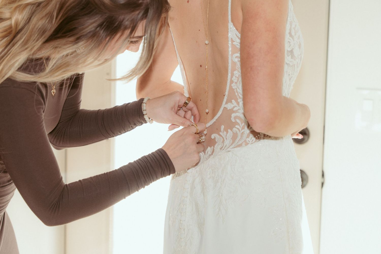 Someone helps with the buttons and final adjustments of a white wedding gown.