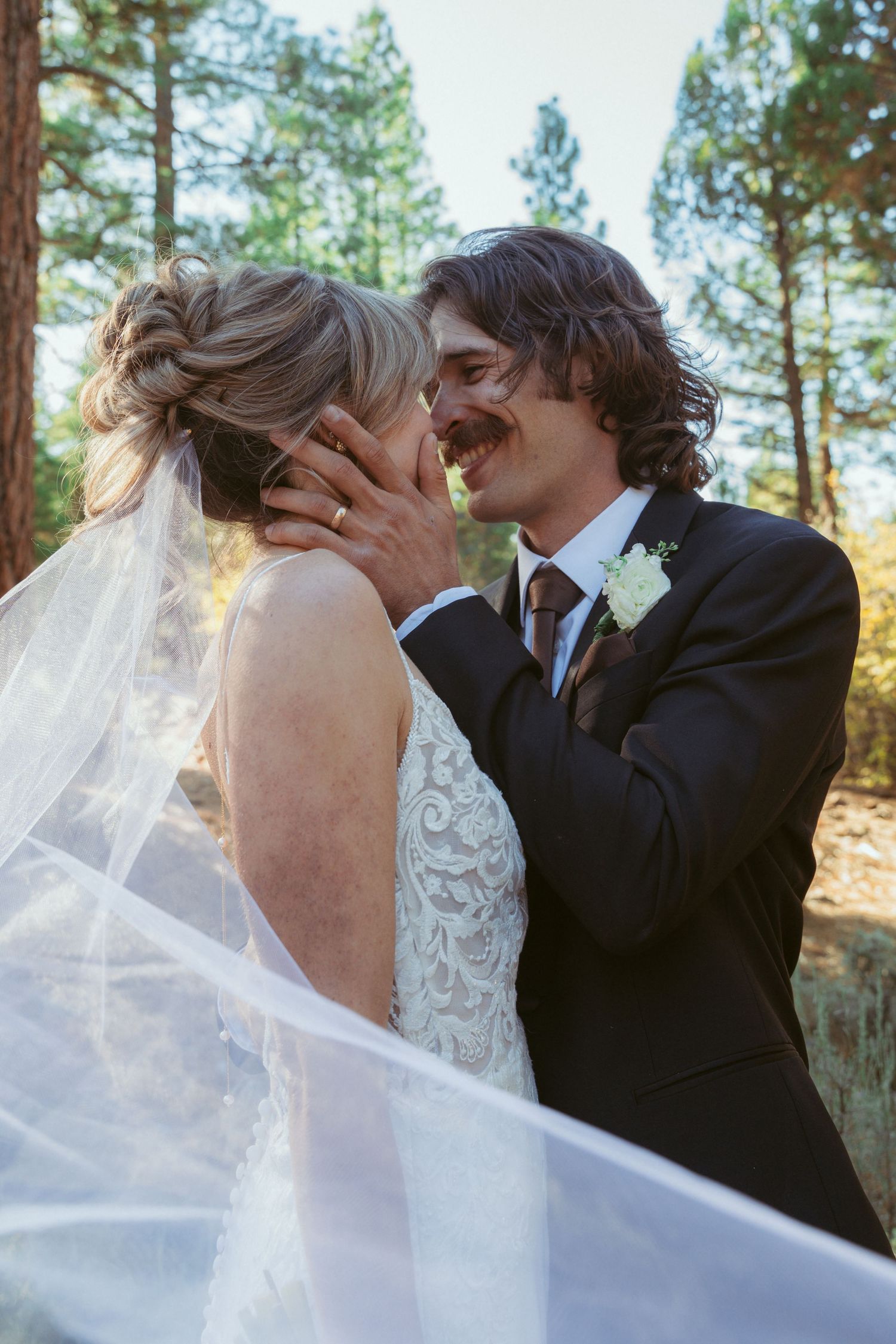 Romantic wedding moment captured in forest with flowing white veil.