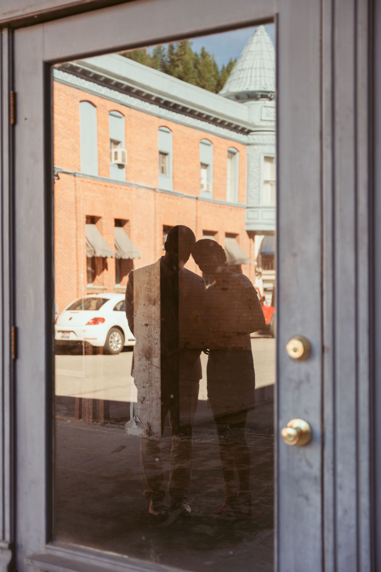 Silhouettes reflected in glass doors of brick building during wedding photoshoot.