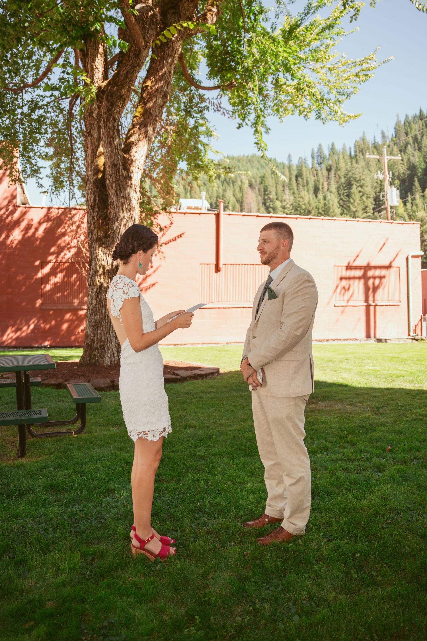 A couple stands under a tree reading letters to each other during their wedding first look.