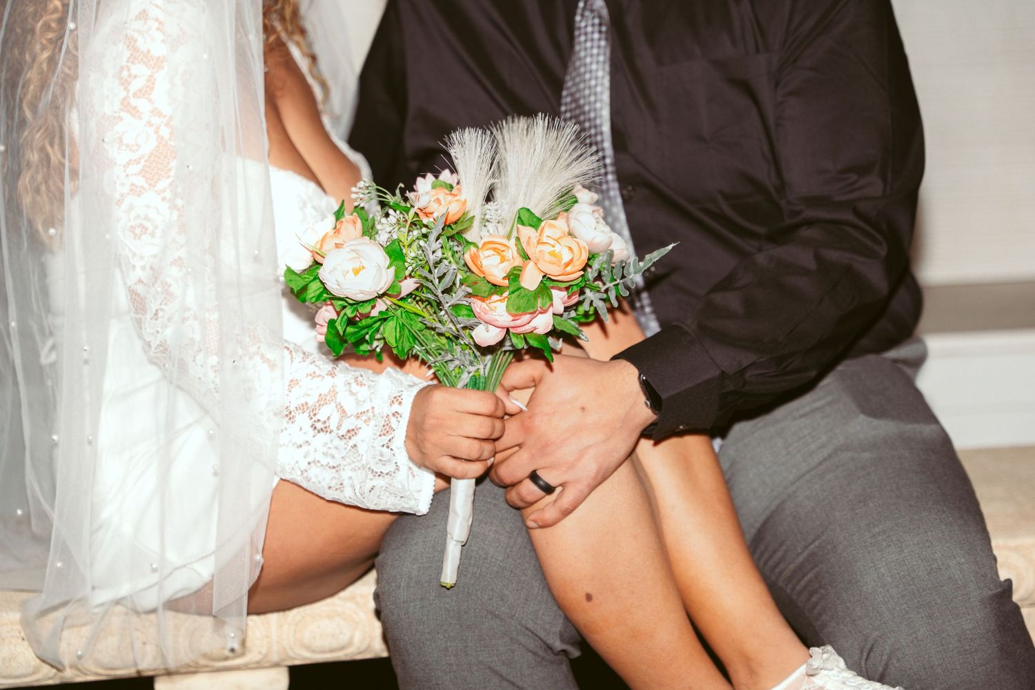 Close-up of couple holding hands with floral bouquet and formal attire.