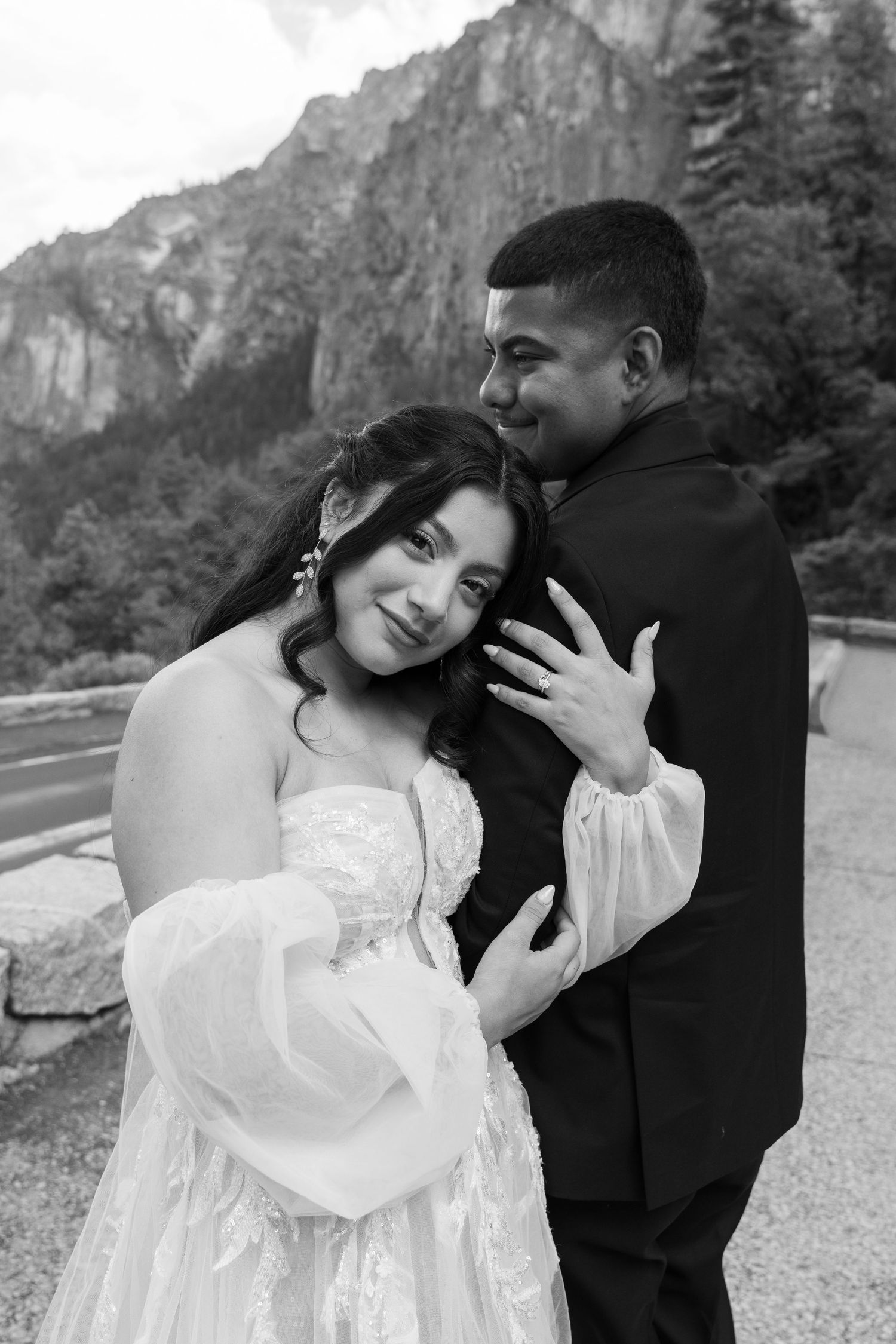 A romantic wedding photoshoot with a couple embracing against a dramatic mountain backdrop in black and white.