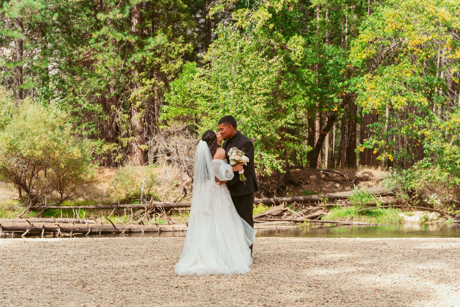 Wedding party poses in a lush green forest setting with natural sunlight filtering through the trees.