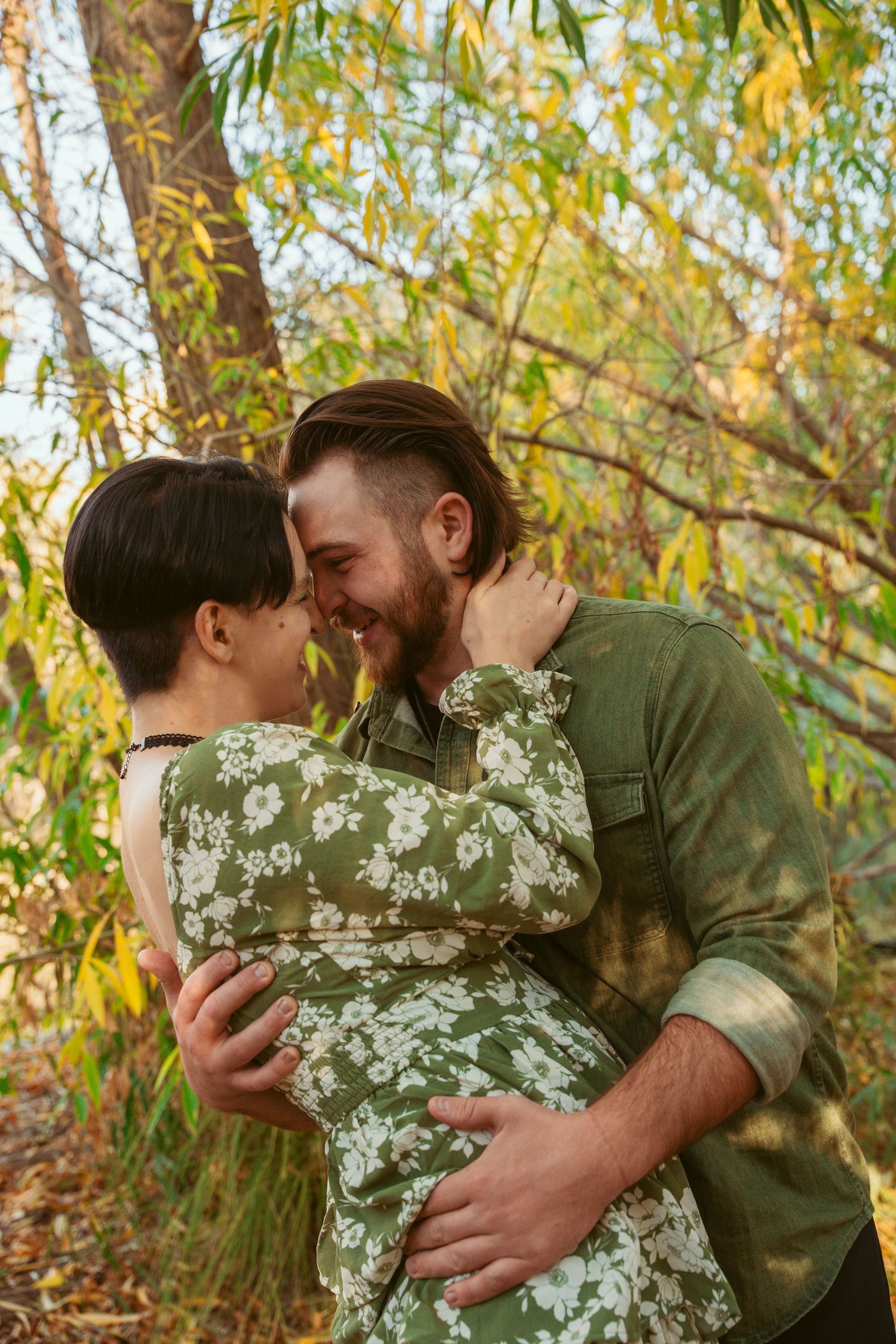 Couple embracing under autumn trees with golden sunlight filtering through leaves.