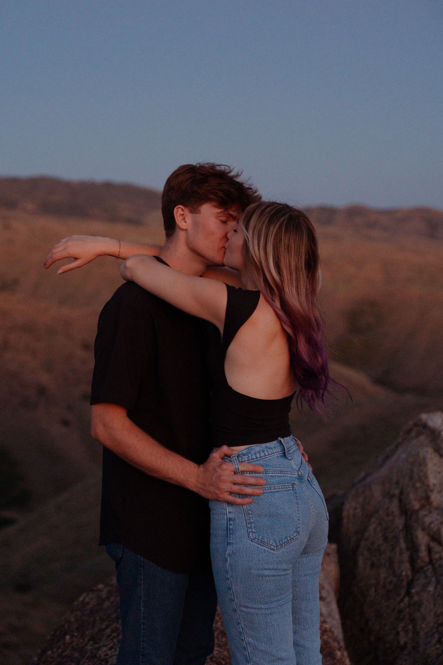 Romantic sunset embrace on mountain overlook with couple in casual attire.