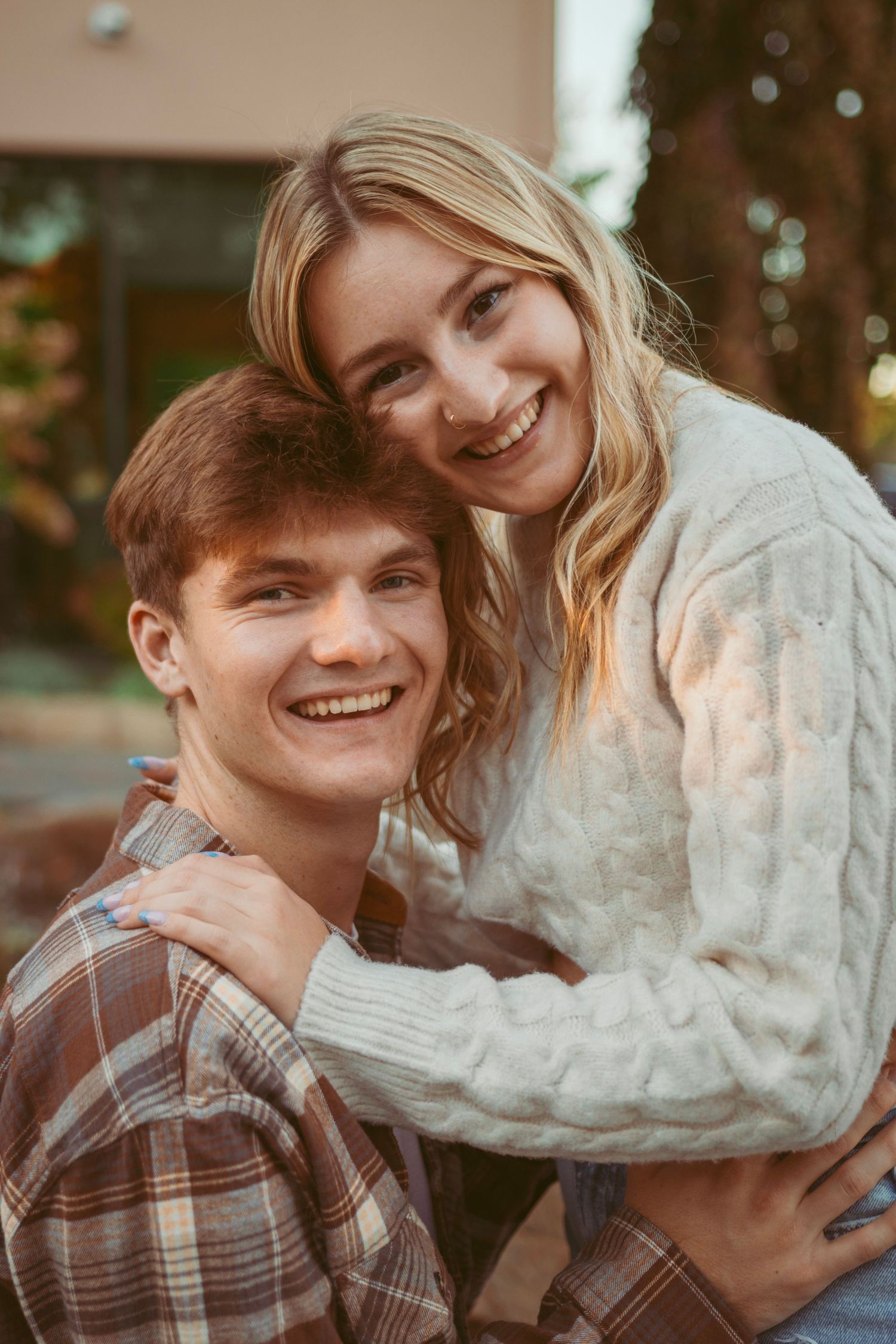 Couple sharing joyful moment outdoors wearing plaid shirt and cream sweater.