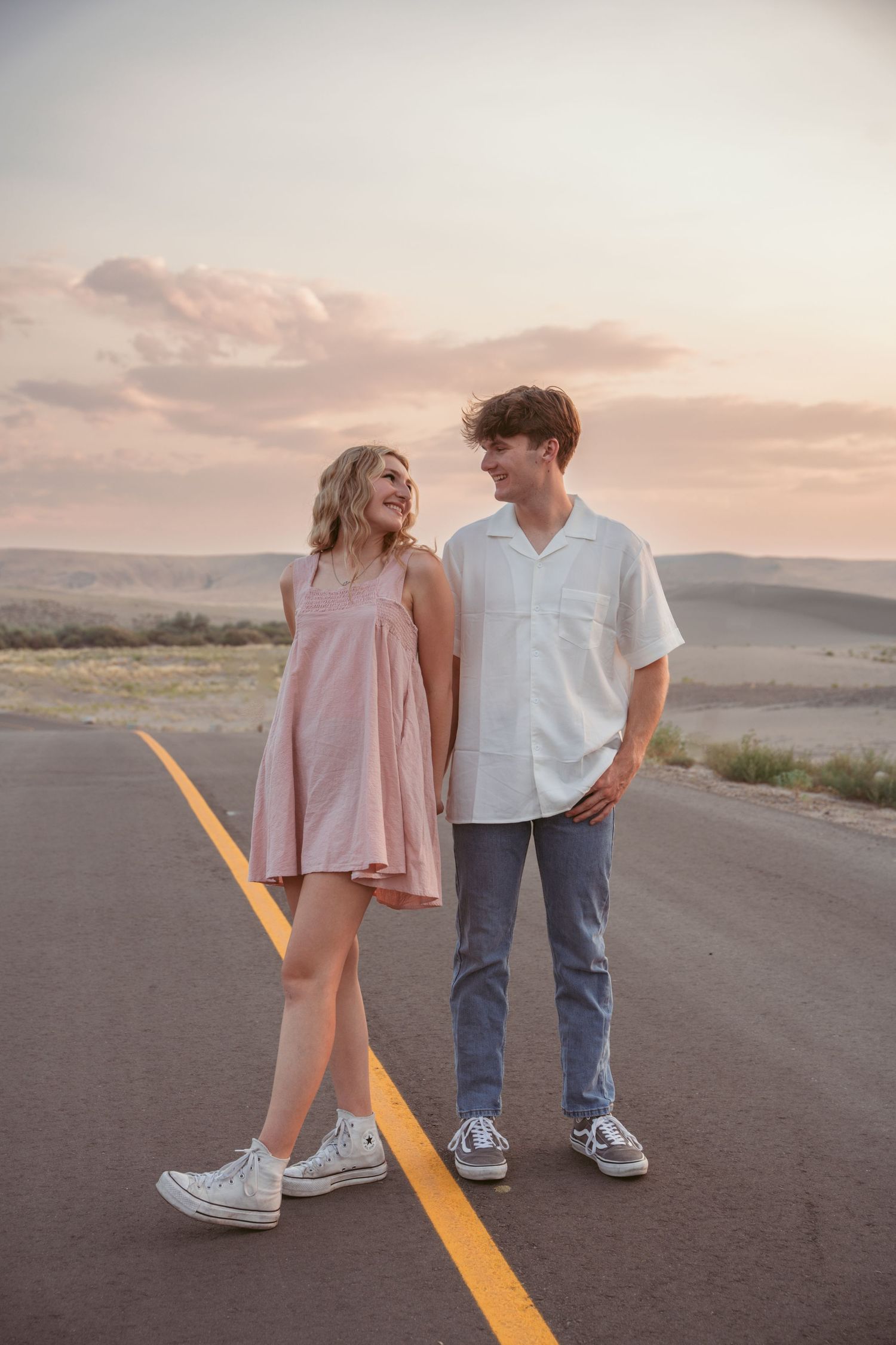 Couple standing on yellow line of desert road during sunset photoshoot.