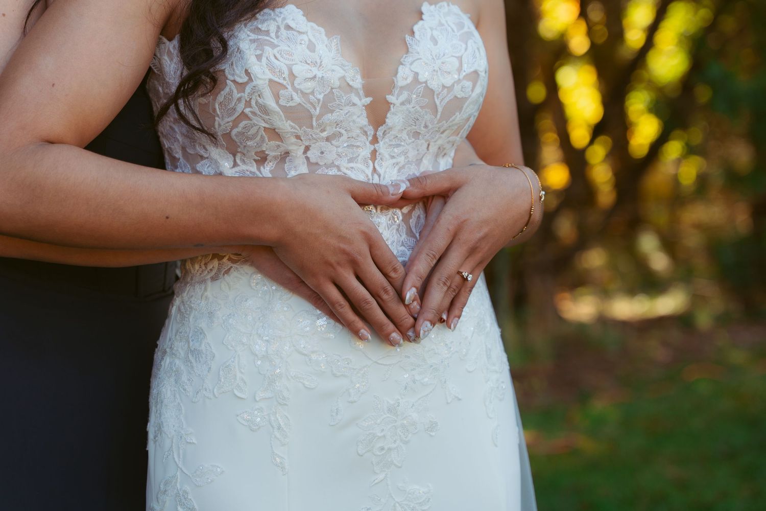 Close-up detail of white lace wedding dress bodice with hands forming heart shape.