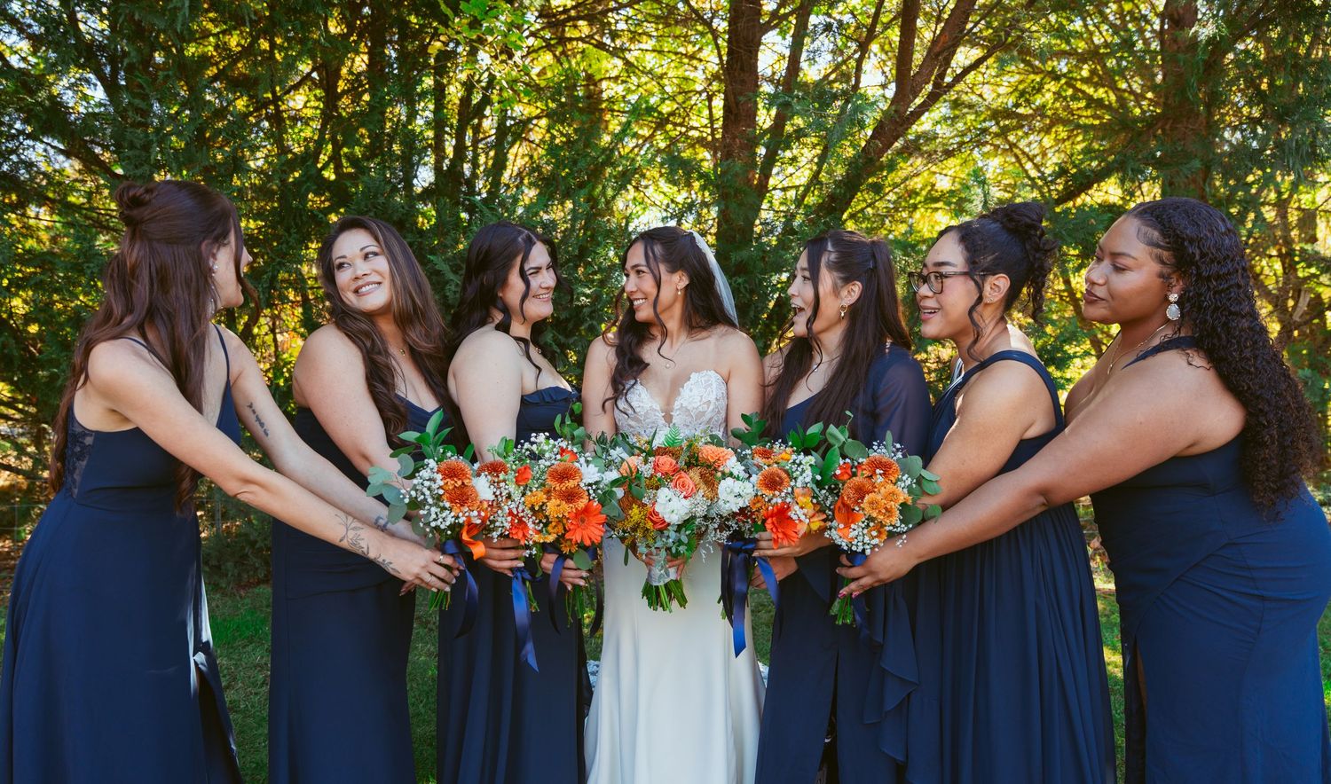 Wedding party members in navy dresses pose with colorful bouquets in outdoor setting.
