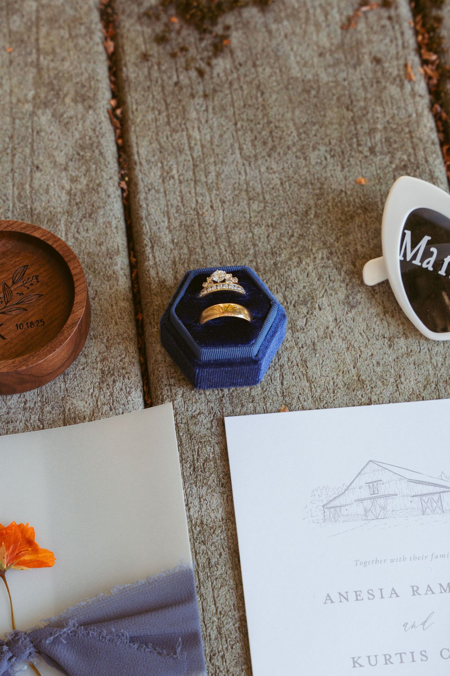 Wedding rings in blue velvet box with invitation and decorative details on wooden surface.