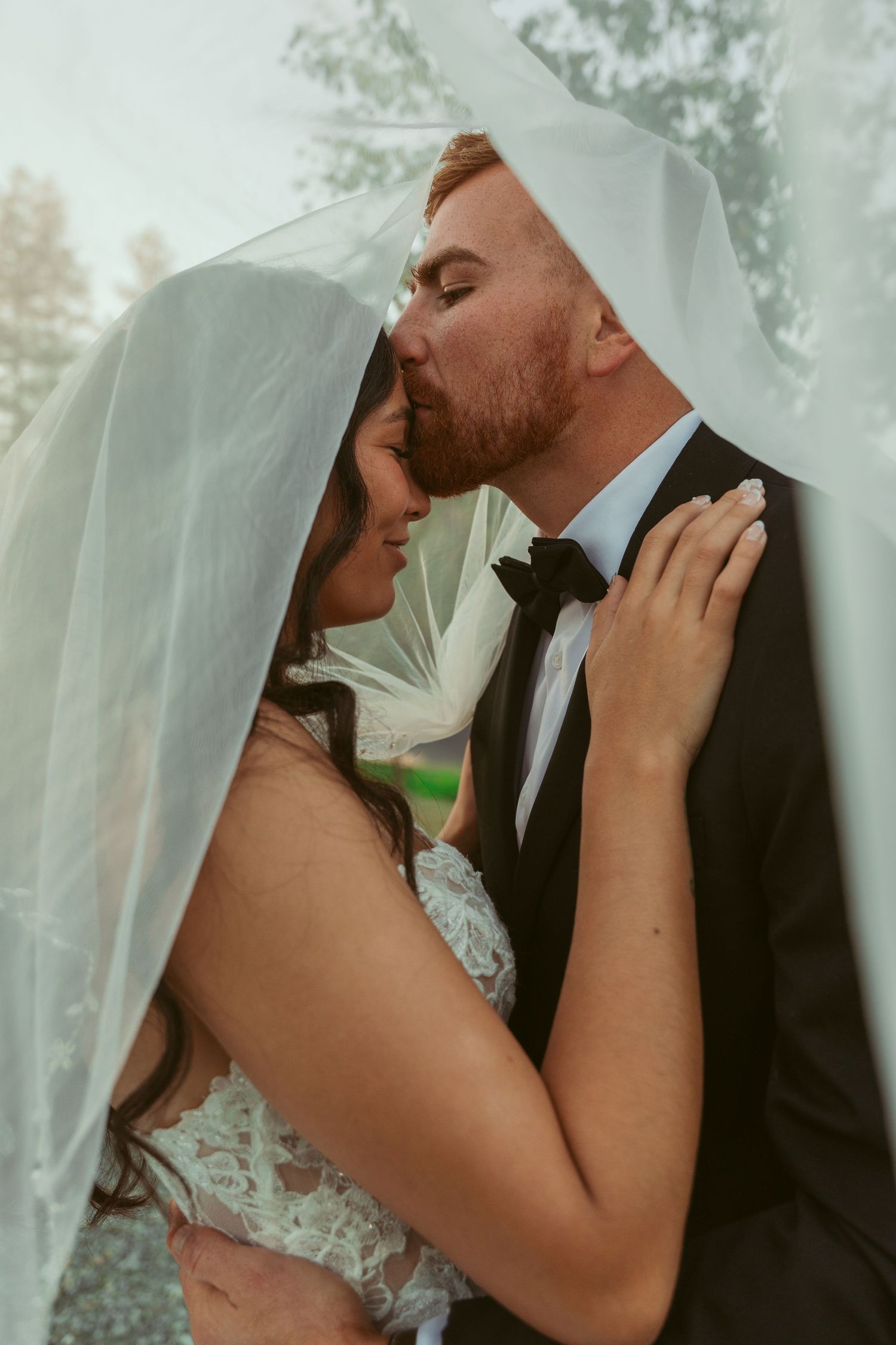 Intimate wedding moment captured under a delicate veil as newlyweds share a tender embrace outdoors.