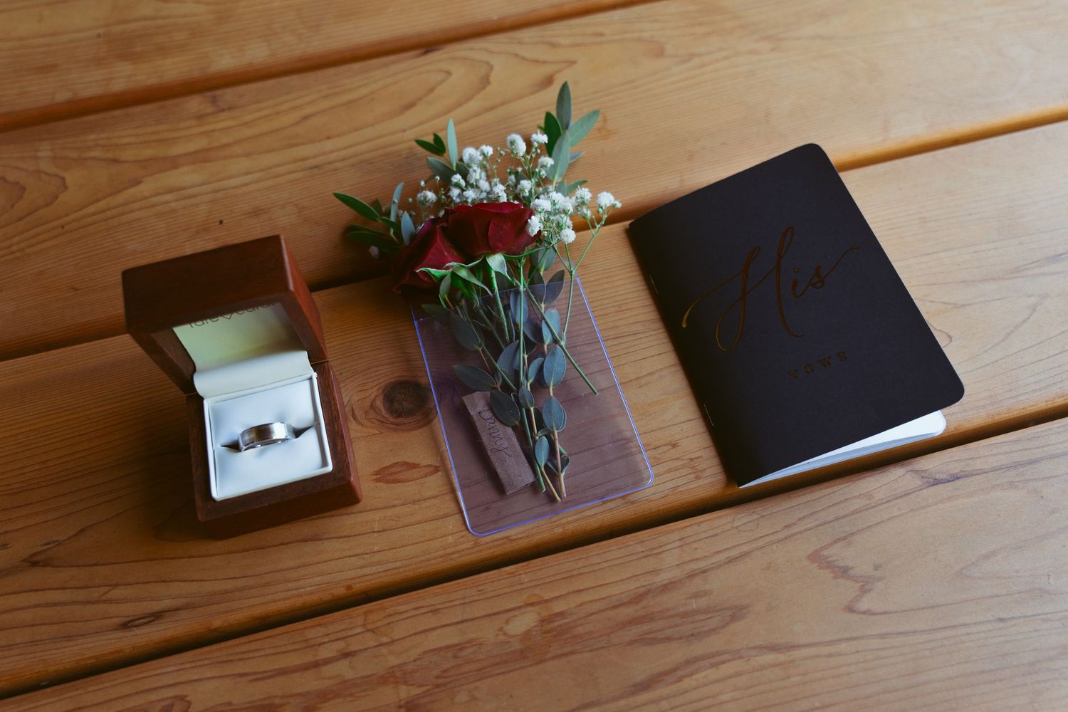 Wedding invitations and red roses arranged on a wooden table.
