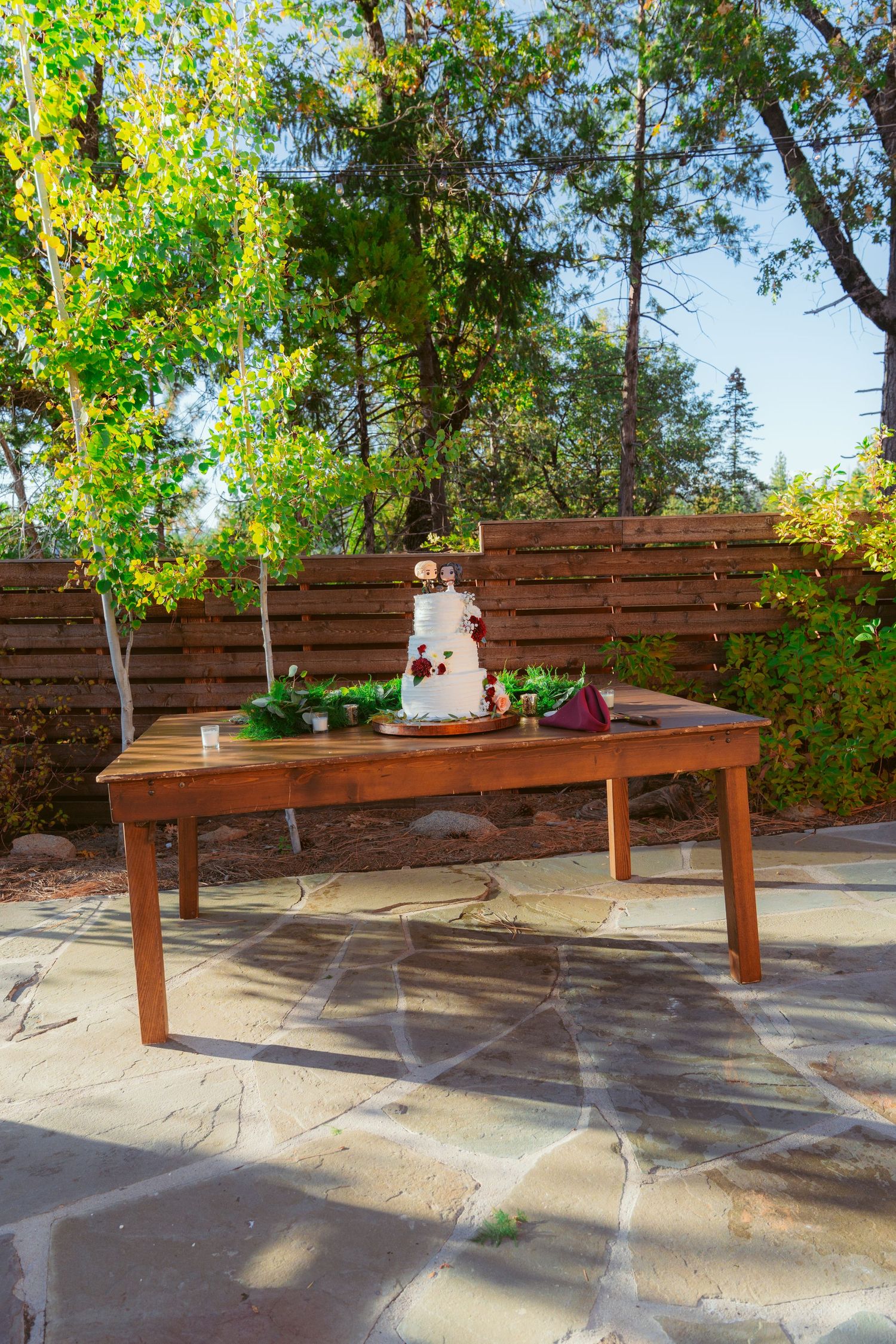 Rustic wooden table displaying wedding cake in outdoor garden setting.