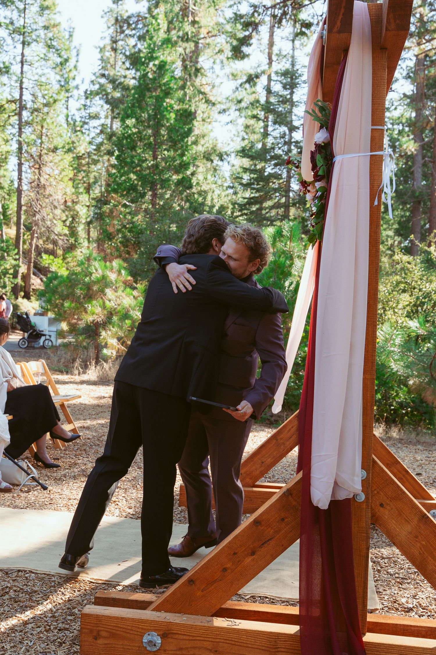 Celebratory moments between wedding party members near wooden arch in forest setting.