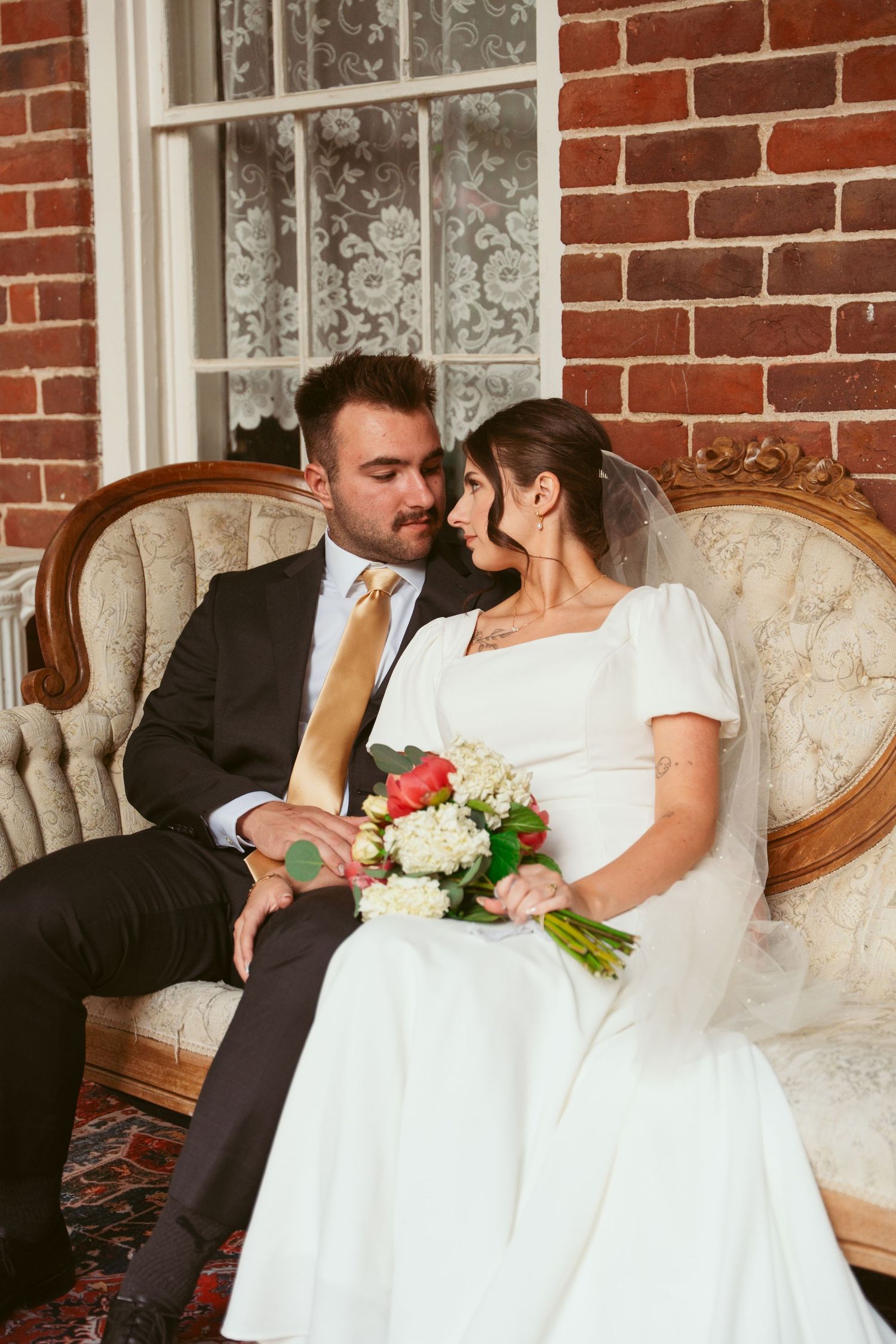 Romantic wedding couple sharing intimate moments on an antique sofa against exposed brick walls.