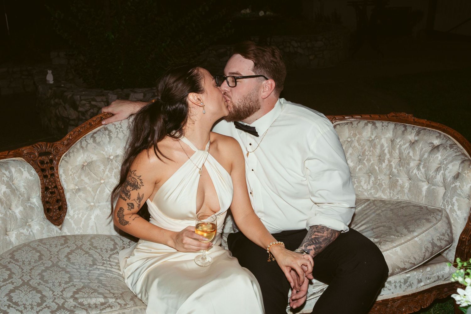 A romantic moment shared between a couple on an elegant vintage sofa during their wedding reception.
