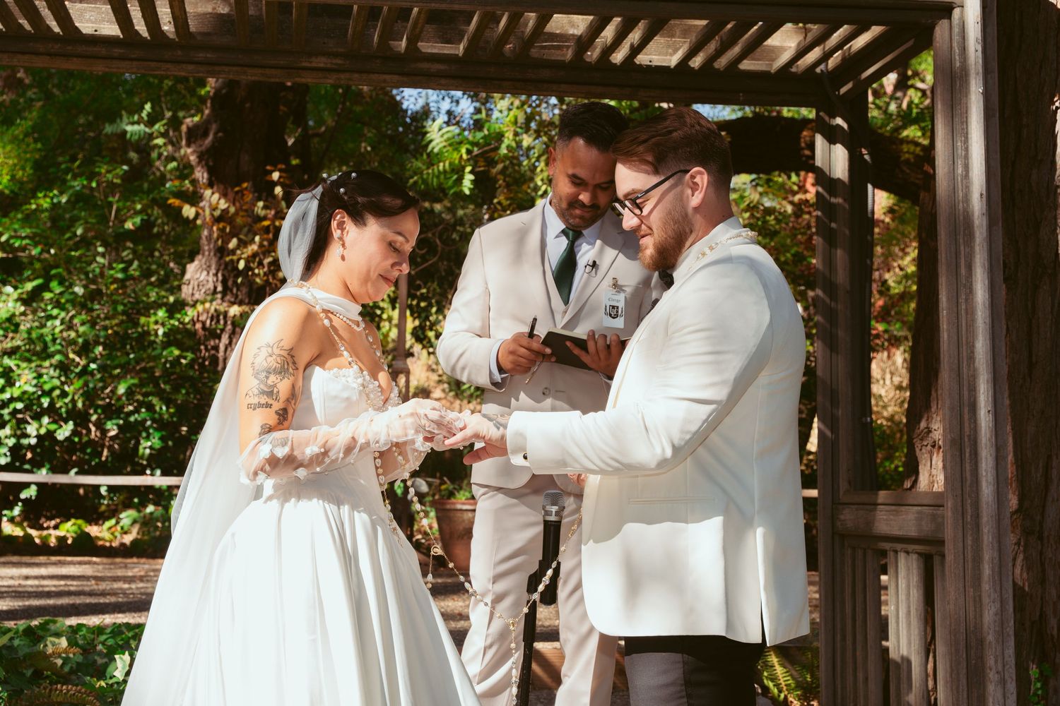 Wedding party gathers under a rustic wooden pergola for celebration photos.