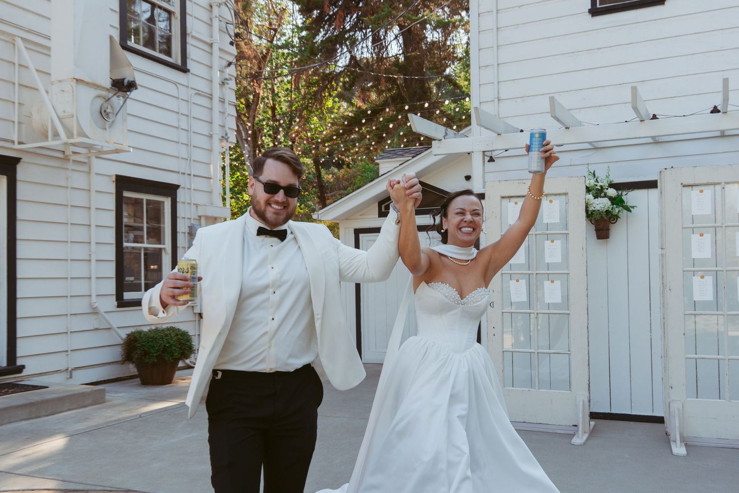Newlyweds celebrating joyfully outside a white building on their wedding day.