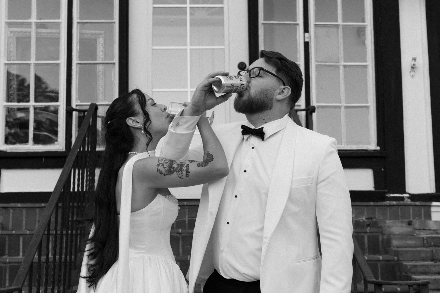Groomsmen in white tuxedos toast with beer bottles at a wedding celebration.