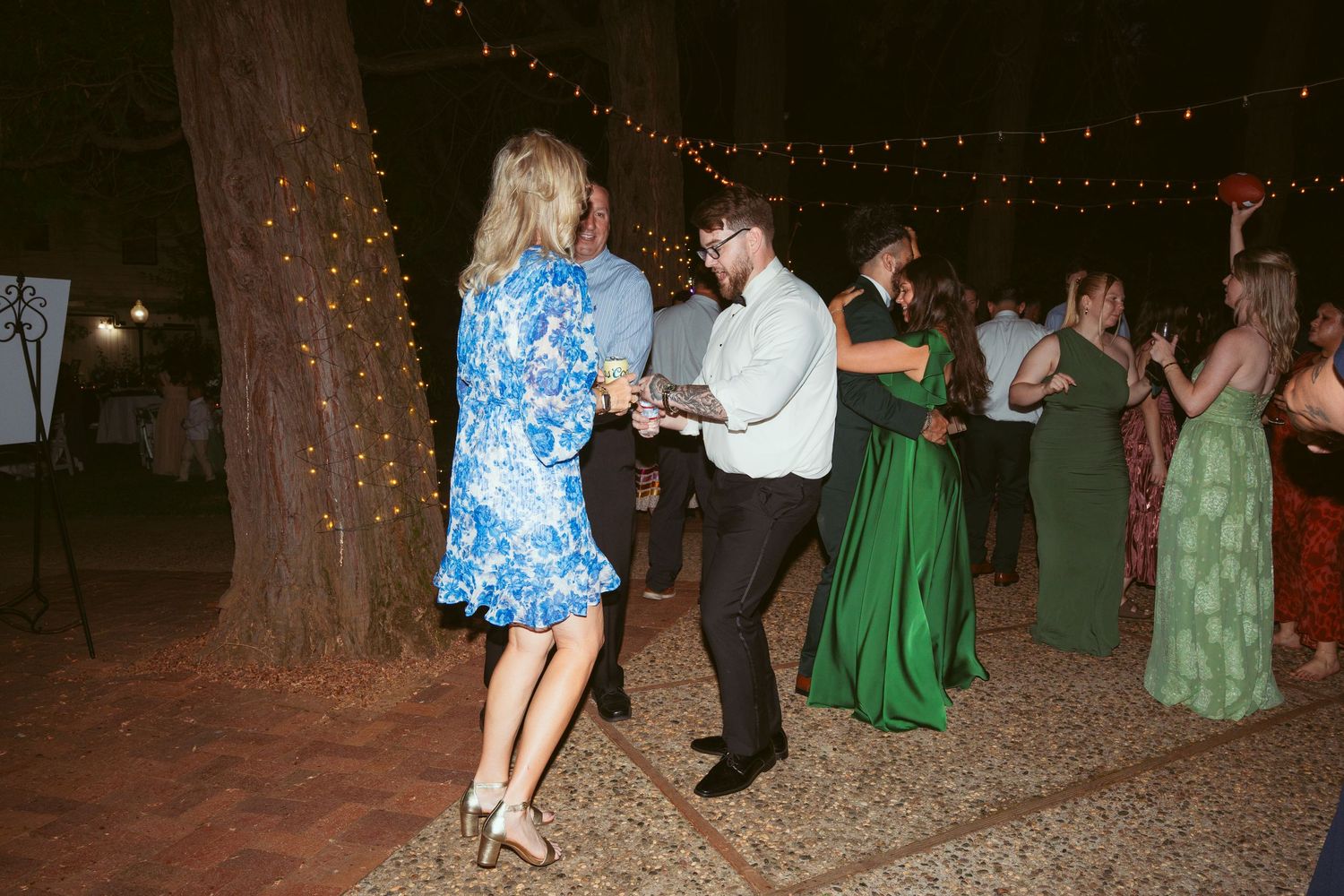 Wedding guests dancing and mingling under string lights at an outdoor evening celebration.