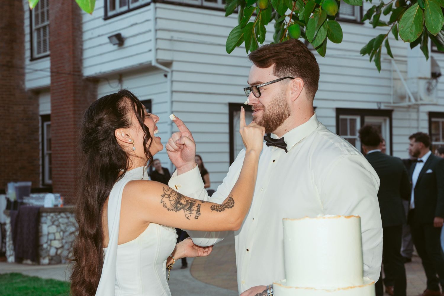A playful moment between newlyweds sharing cake during their outdoor wedding reception.