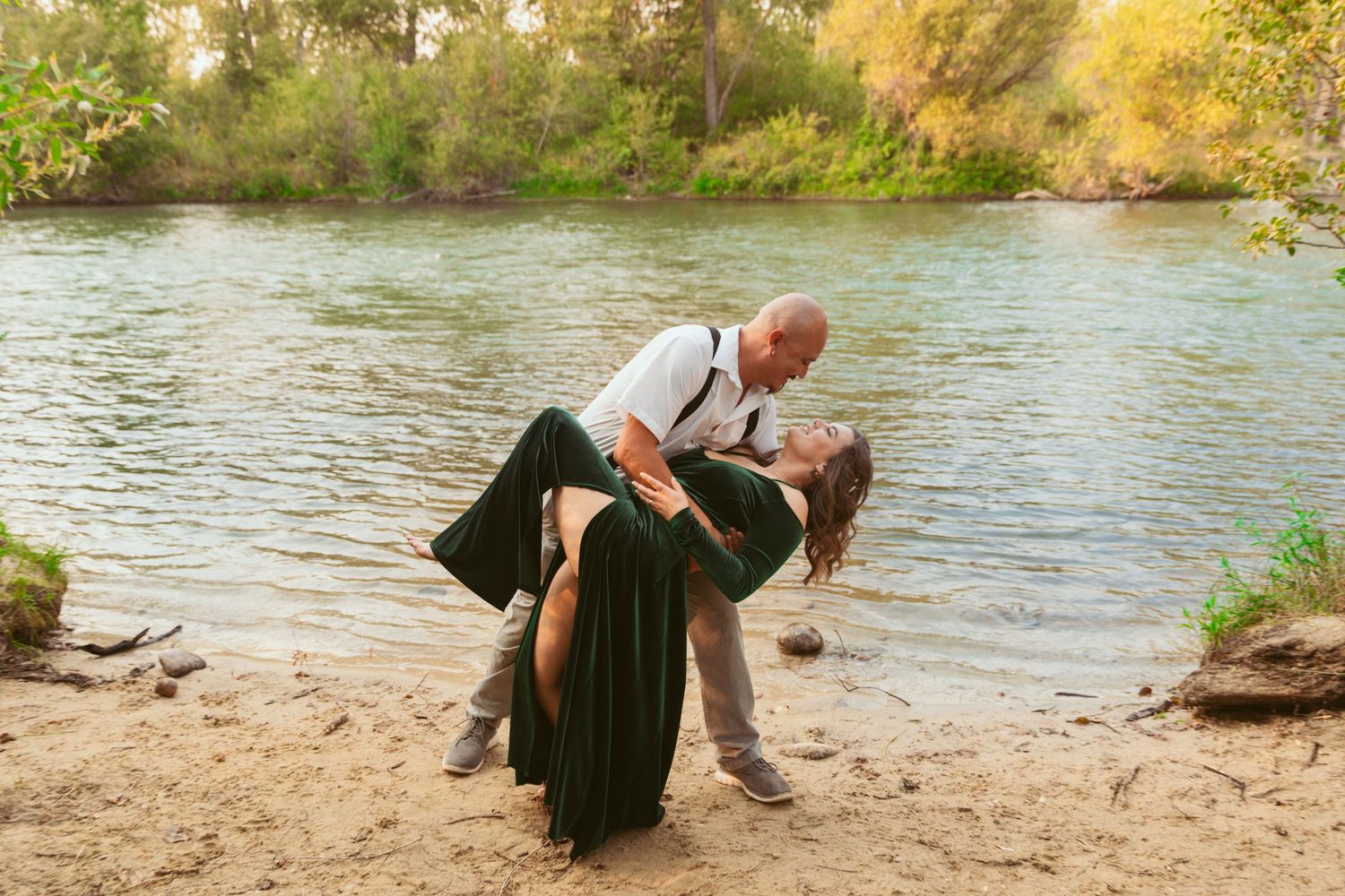 Couple embracing by a riverbank during sunset in a natural setting.