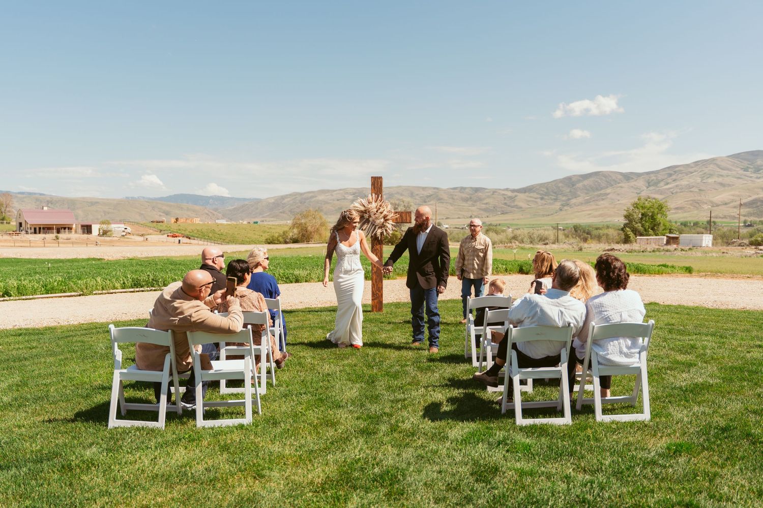 A small outdoor wedding ceremony with white chairs arranged on a grassy lawn against mountain scenery.