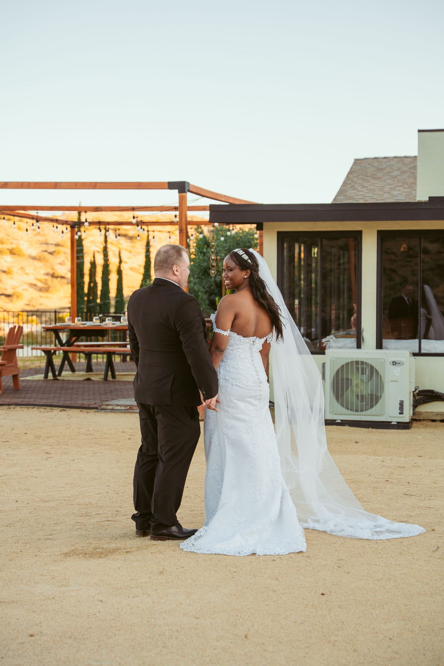 Wedding couple photographed against desert landscape with buildings and mountains in background.