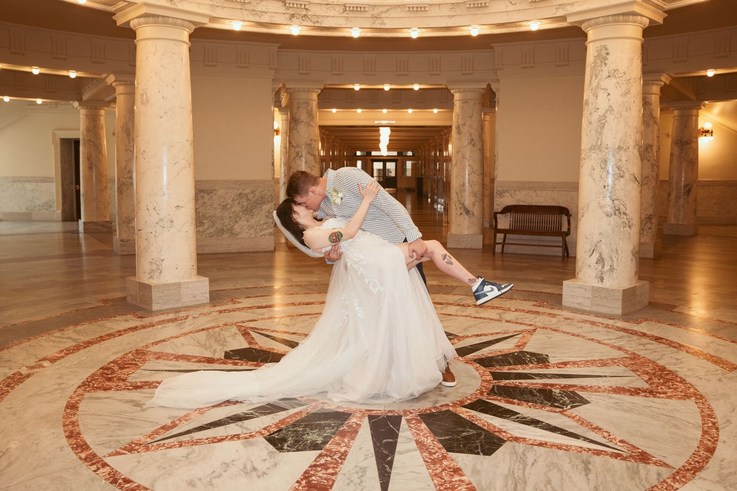 Wedding couple dancing in an elegant marble-columned ballroom with decorative floor pattern.