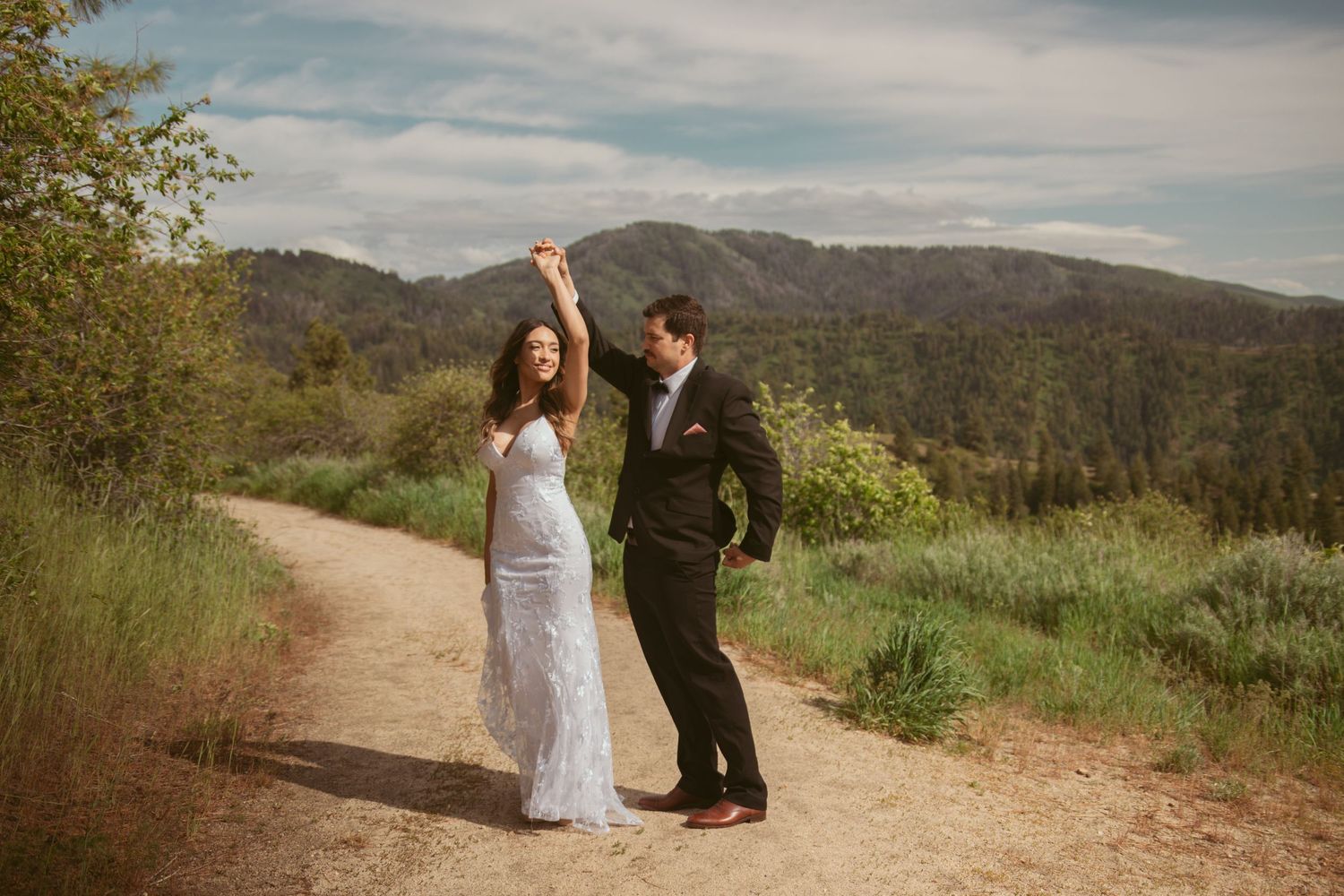 Two people dance together on a dirt trail with mountains and blue skies in the distance.