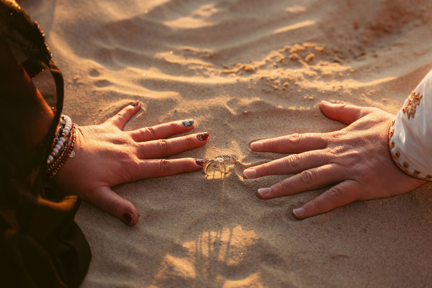 Hands reaching toward each other against a sunset beach background.
