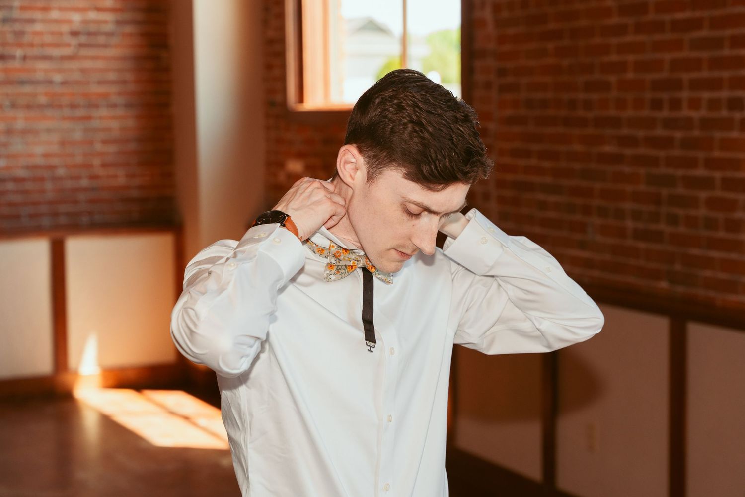 Groom getting ready in a white dress shirt against a brick wall background.