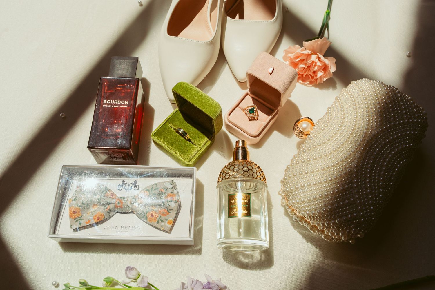 Wedding accessories including bow tie, perfume, shoes, and ring boxes in natural light.