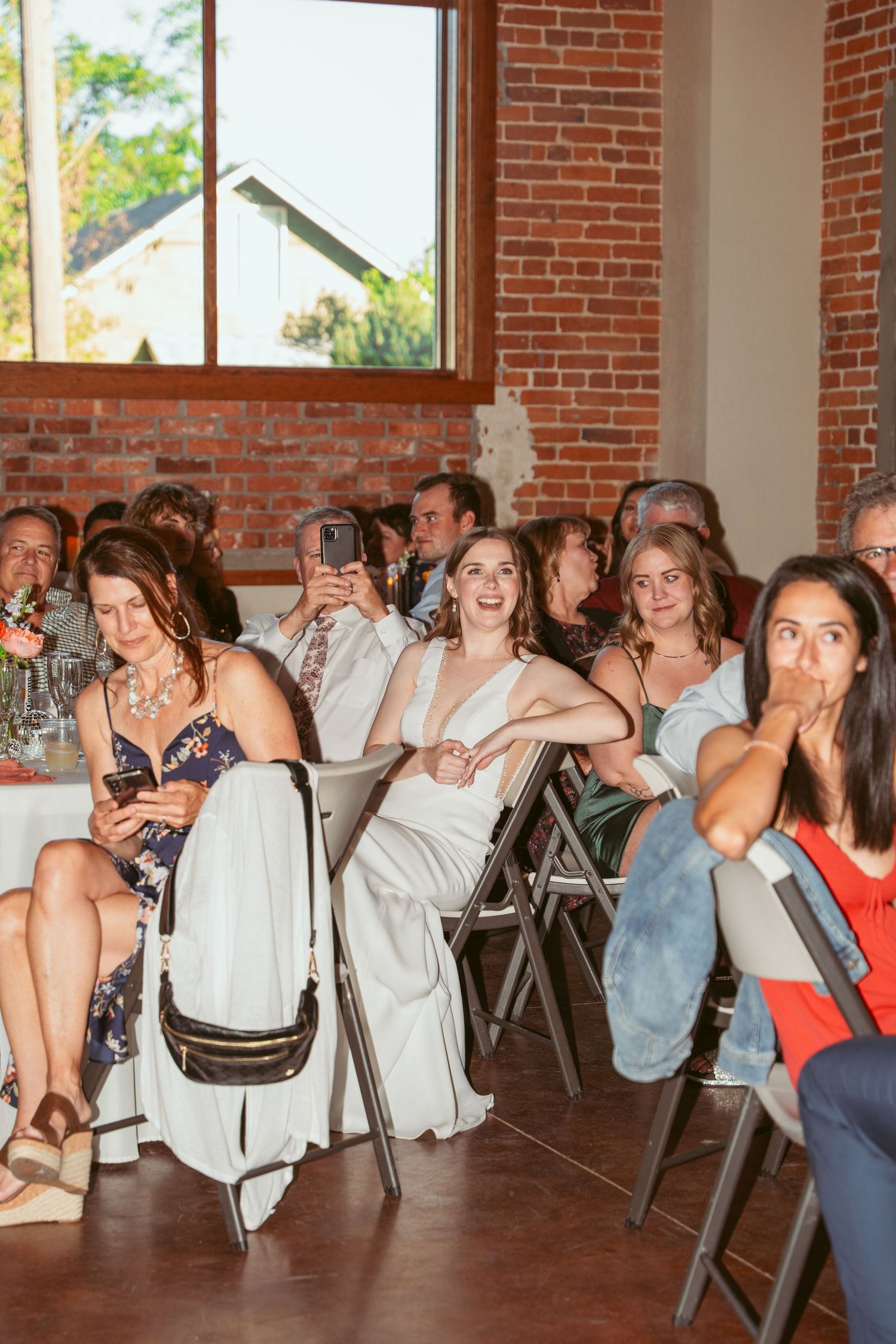 Wedding guests seated at tables laugh and smile during reception festivities.