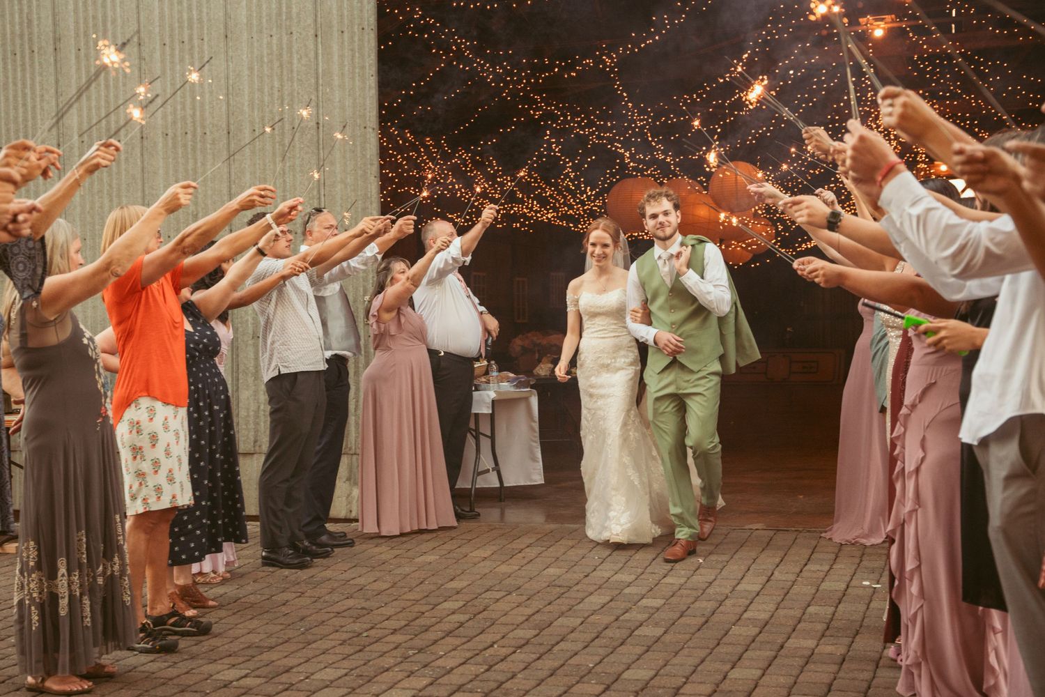Guests line up holding sparklers as couple walks through during evening wedding reception.