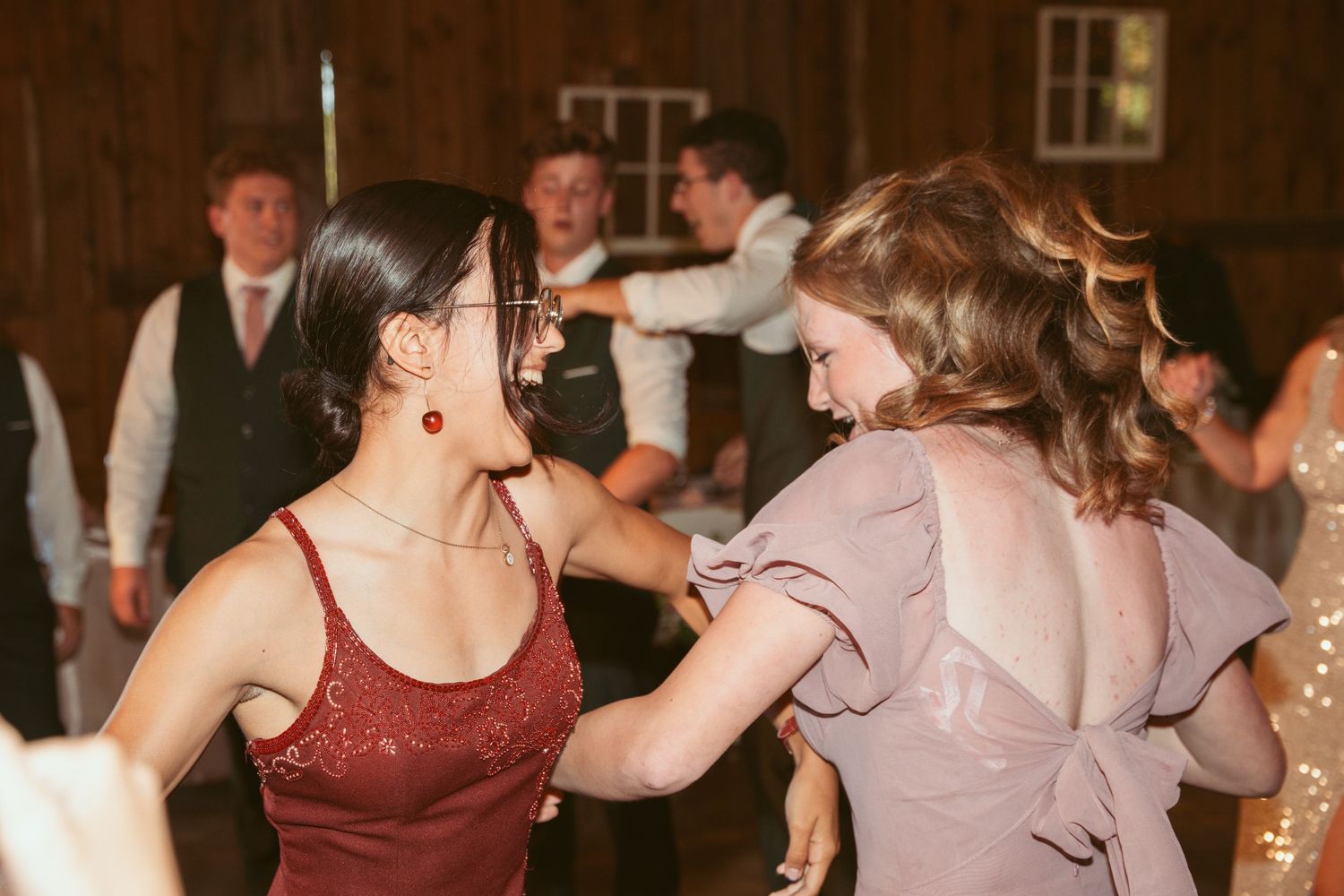 Wedding guests share a fun dancing moment under warm lighting at a rustic barn reception.