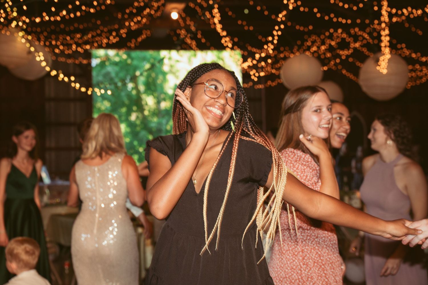 Guests dancing joyfully under warm string lights and paper lanterns at a rustic indoor reception venue.