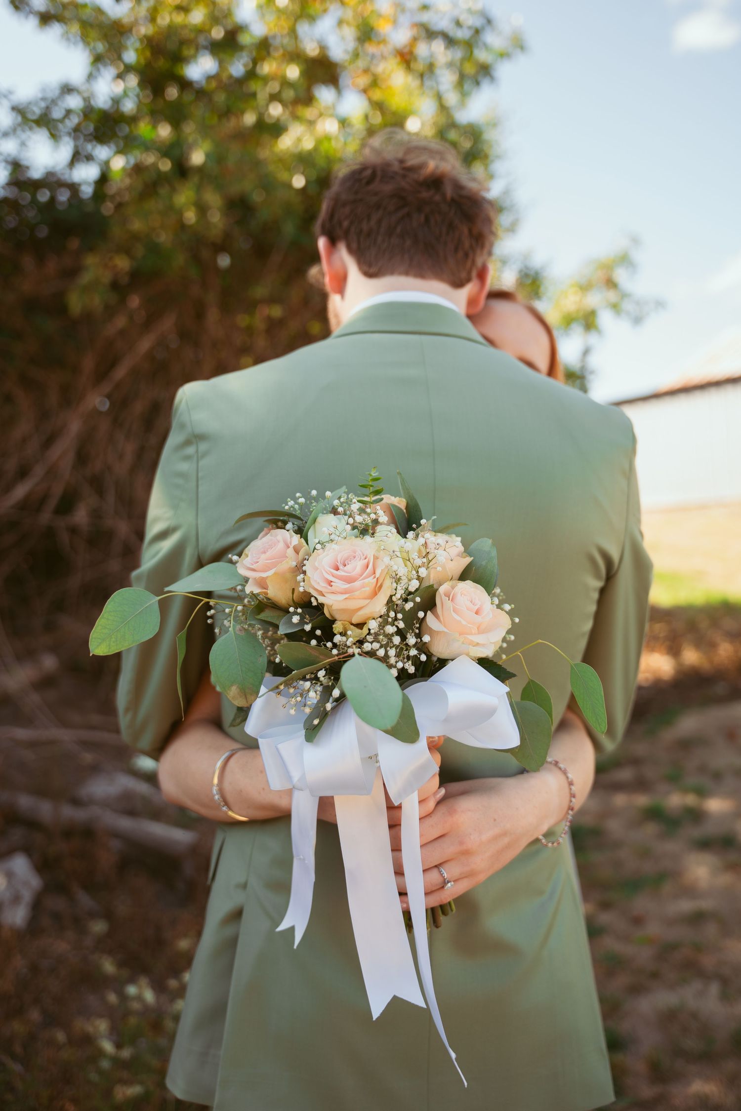 Close-up of groomsmen wearing sage green suits with pink and white floral boutonnieres.