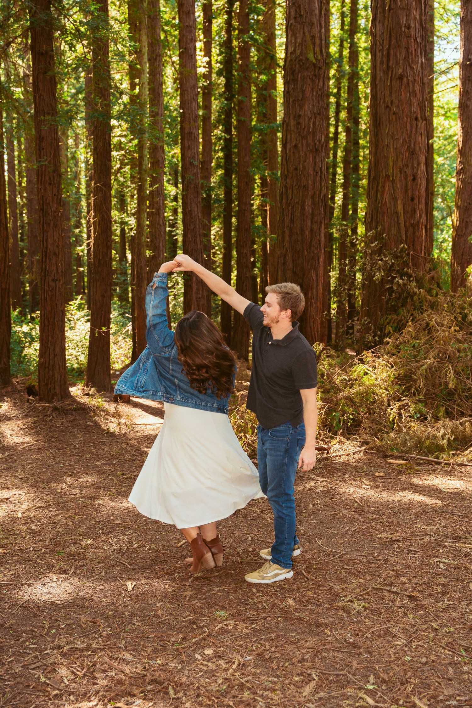 Two people share a dramatic dance pose in a sunlit redwood forest clearing.