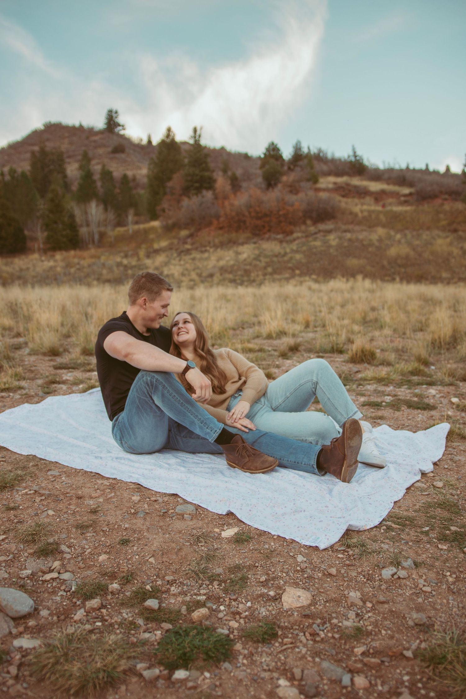 Intimate couple laying together on blanket in rustic mountain setting during autumn.