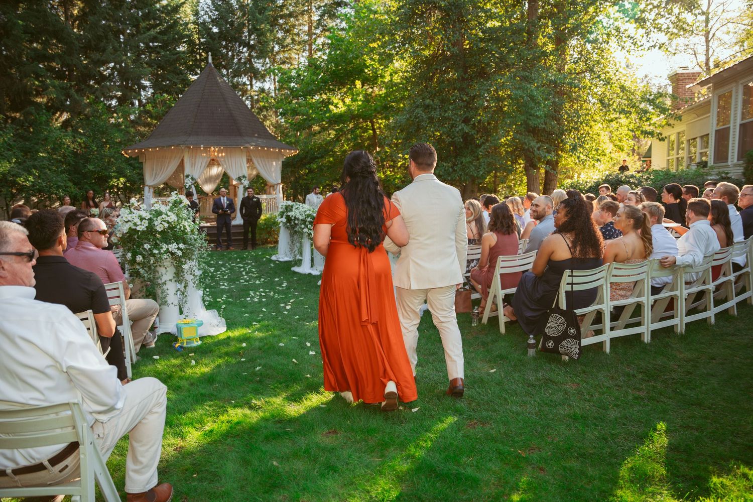 Wedding guests seated on white chairs during an outdoor garden ceremony.