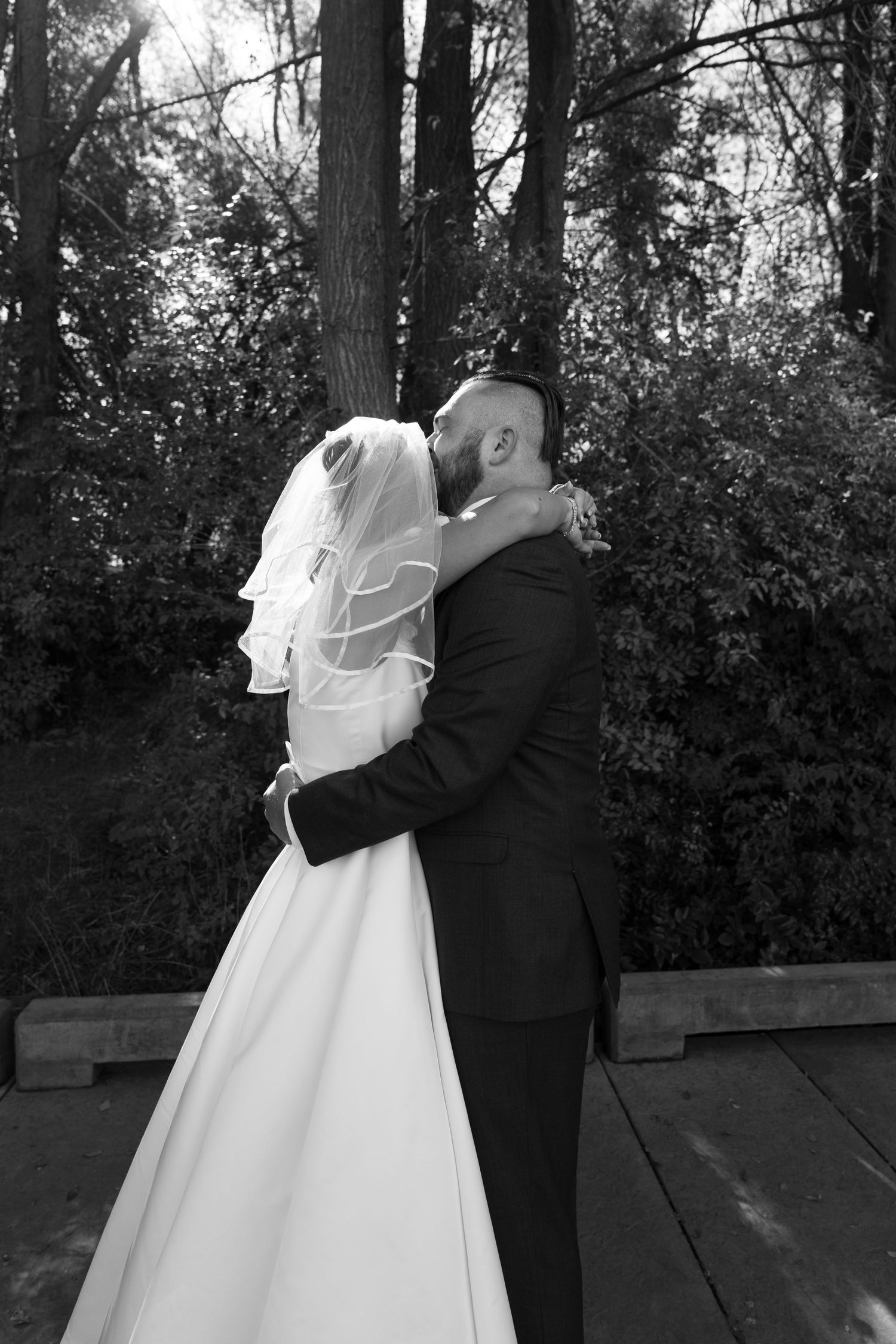 Black and white wedding photo capturing an intimate moment between a couple on a wooden deck.