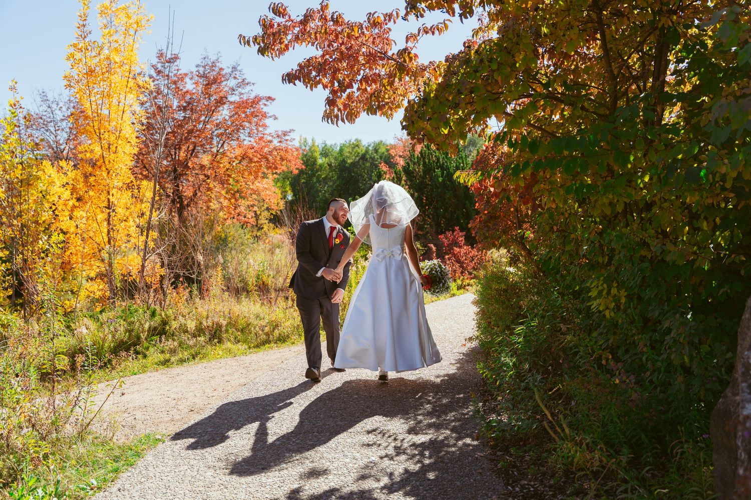 Wedding party walking along a path surrounded by vibrant fall foliage.