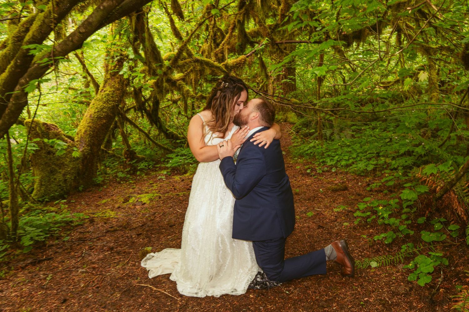 Wedding couple shares tender moments on a forest path surrounded by towering trees.
